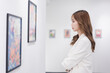 © Kiattisak - Woman visiting art gallery her looking pictures on wall watching photo frame painting at artwork museum people lifestyle concept.