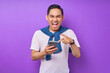 © Bangun Stock Photo - Excited young Asian man in casual t-shirt pointing fingers at mobile phone, reacting to new app isolated on purple background. People lifestyle concept