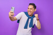 © Bangun Stock Photo - Excited young Asian man in white t-shirt using smartphone and making winner gesture isolated on purple background