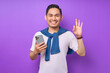 © Bangun Stock Photo - Smiling young Asian man in white t-shirt using smartphone and showing ok okay gesture isolated on purple background