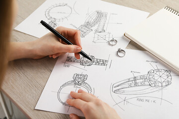 Wall Mural - Jeweler drawing sketch of elegant ring on paper at wooden table, closeup