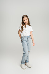 Poster - Full length of preteen girl in jeans and t-shirt posing and smiling on grey background.