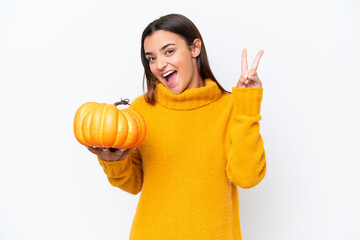 Poster - Young caucasian woman holding a pumpkin isolated on white background smiling and showing victory sign