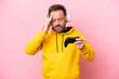 Middle age man playing with a video game controller isolated on pink background with headache