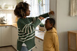 © DimaBerlin - Caring african american mother measures changes height of child son on wall with pencil at home. Interested kid boy stand with mom wait for result hopes become taller tracking increase noting growth