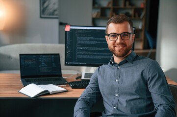 Software developer is sitting and posing. Man in formal clothes is working in the modern office. Using computer