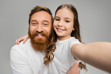 Wall Mural - Smiling preteen kid hugging bearded dad in white t-shirt isolated on grey.