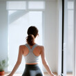 Yoga and sport. Back view of slender young woman in sportswear sitting in lotus position doing yoga. Peaceful girl relaxes in lotus position at home or gym sitting facing windows on floor on yoga mat.