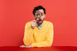 scrupulous man in yellow long sleeve jumper holding magnifying glass on red coral background.