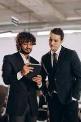 Wall Mural - Curious businessmen watching video on tablet. Indoor shot of coworkers in black suits using digital gadget in office