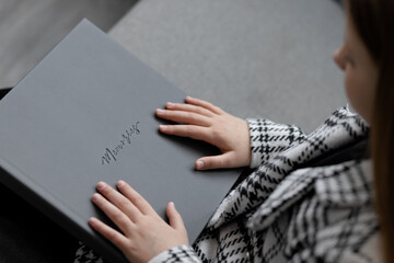 Photo of a gray leather photo book with the inscription memories in the hands of a 10-year-old girl. Close up