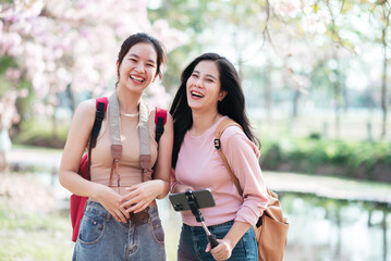 Two young people travelling with happy, Smiling asian woman friends with backpack and camera traveling in the park on vacation summer.