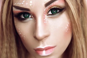 young attractive cute girl with an unusual creative make-up of wild deer. halloween ideas of beauty 