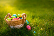 Easter Eggs In Basket In Grass. Colorful Decorated Easter Eggs In Wicker Basket. Traditional Egg Hunt For Spring Holidays. Morning Magical Light. 