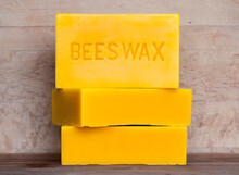Three Bricks Of Pure Bees Wax Stacked Against A Wood Background