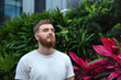 © Евгений Шемякин - Portrait of happy young bearded man with beard breathing deep, inhale fresh air on natural background, green wall with leaves, flower in tropical country in garden. Eco, ecological concept.