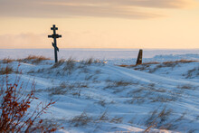 Snow-covered Cemetery In The Tundra On The Shore Of The Frozen Sea.  An Old Cemetery In The Far North Of Russia In The Arctic. View Of The Cross And Graves. Cold Winter Weather. Chukotka, Siberia.