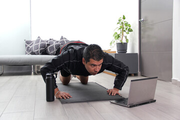 Overweight latino adult man exercises inside his home in his living room via computer online to be healthy