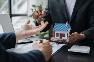 Wall Mural - Real estate agents, insurance sales agents, and young Asian businessmen handing home keys and model homes to homebuyers after signing sales contracts are satisfied in the office.