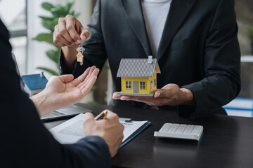 Real estate agents, insurance sales agents, and young Asian businessmen handing home keys and model homes to homebuyers after signing sales contracts are satisfied in the office.