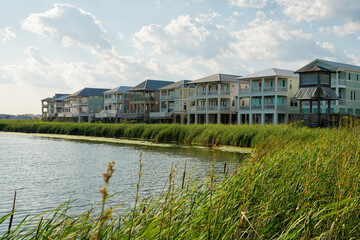 Wall Mural - Row of houses under the bright sky with clouds with lagoon waterfront at Destin, Florida. There is a lagoon at the front with tall grasses near the shore and a boardwalk pavilion on the right.