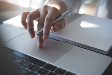 Wall Mural - closeup of woman hand typing, searching the information on laptop computer with a pen and notebook o
