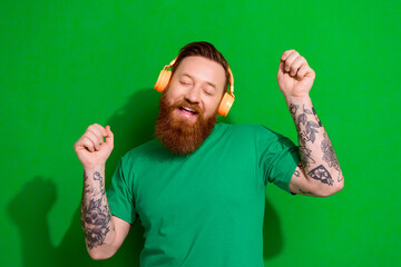 Wall Mural - Photo of good mood nice guy with ginger beard dressed stylish t-shirt headphones listening playlist isolated on green color background