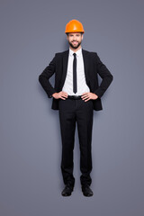 Sticker - Full length size portrait of attractive cheerful joyful investor in orange hard hat and black tuxedo with tie, looking at camera, isolated on grey background, holding two arms on waist