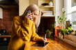 © baranq - Adult woman writing on tablet while talking on the phone in a kitchen