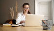 © muse studio - A businesslike woman with glasses using a laptop computer in the office. The manager in a white shirt clicks on the display.