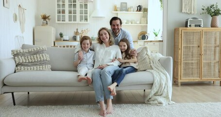 Wall Mural - Cheerful parents hugging cute preschool kids, resting on sofa, smiling, laughing, enjoying leisure time together, affection, family relationship, closeness. Happy couple and children home portrait