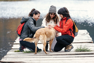 Pretty family playing with a dog wihile staying on a pier on the lake