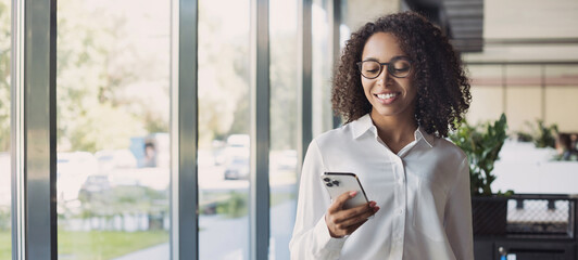 Business woman using smartphone in modern office, banner. Student girl texting on mobile phone indoors. Communication, connection, mobile apps, technology, business lifestyle concept