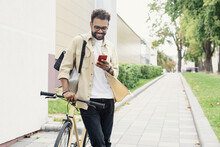 Young handsome man walking with bike and smartphone in a city, Smiling student men with bicycle smiling and looking at mobile phone, Modern lifestyle, connection, travel, casual business concept