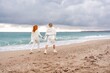 © svetograph - Women sea walk friendship spring. Two girlfriends, redhead and blonde, middle-aged walk along the sandy beach of the sea, dressed in white clothes. Against the backdrop of a cloudy sky and the winter