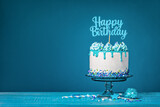 Fototapeta Tęcza - White happy birthday cake with teal ganache over a blue background