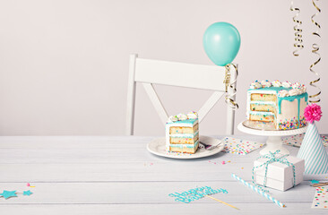 Birthday party table setting with slice of vanilla confetti cake and decorations on a light grey white background