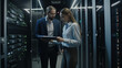 © LAYHONG - A man and a woman stand in a server room with tablet. Generative AI