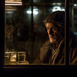 Generative AI - A homeless man looking out a window at a glass of water and a light in the background is a lit candle, cinematic photography, a character portrait, art photography