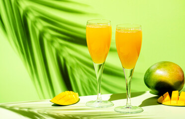 Wall Mural - Mango bellini alcoholic cocktail drink with prosecco or champagne, mango puree, syrup and ice. Green background, hard light, shadow pattern