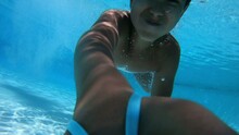 The Boy Dives Into The Pool With Blue Water Has Fun And Swims Underwater