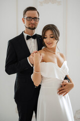 Wall Mural - groom in a black suit tie and the bride in a bright studio