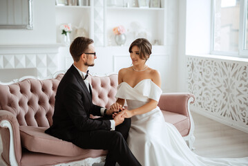 Wall Mural - groom in a black suit tie and the bride in a bright studio