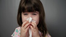 Little cute girl blows her nose in a napkin, seasonal allergies, rhinitis in a child. Closeup isolated portrait of a little girl, sick with a cold, ODS.
