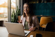 © Studio Dva Kera - Young woman in a restaurant, engaged in a video call on her laptop with a big smile on her face.