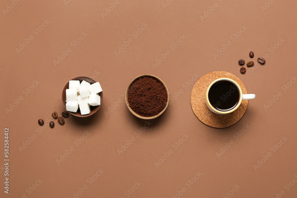 Bowls with coffee powder, sugar and cup on brown background