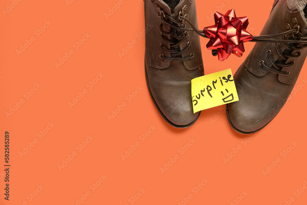 Paper with word SURPRISE, boots and bow on red background. April Fools' Day celebration