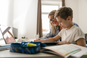 Happy mom and son doing homework and studying with laptop together. Home education