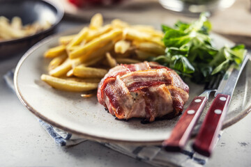 Wall Mural - Bacon wrapped meat served with french fries and salad on a plate with cutlery