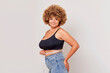 © South House Studio - Cute young curly woman in black top with measurer on her waist stands half turned on light background, student plus size is happy about diet results, healthful lifestyle, copy space, high quality